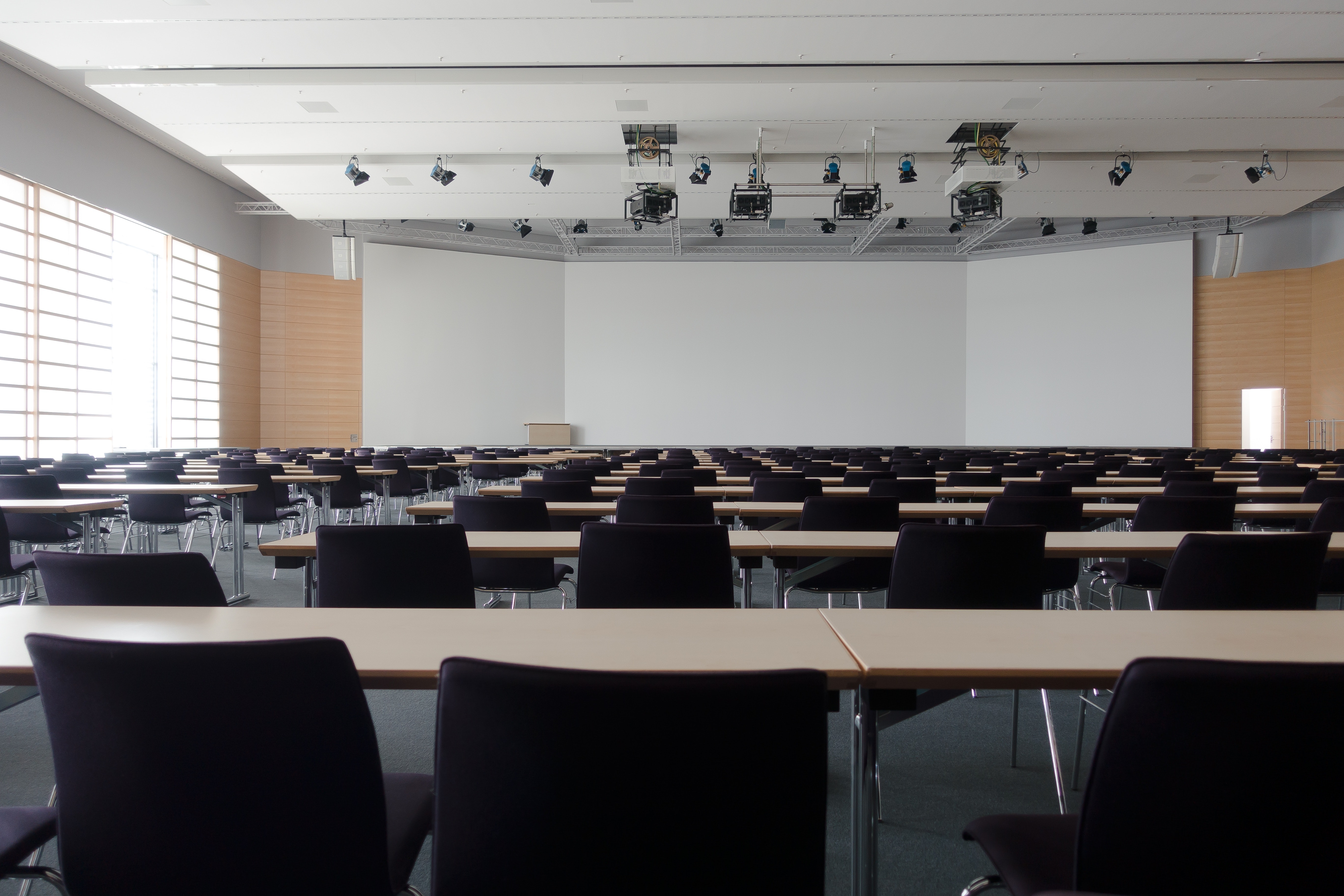 Empty classroom with long rectangular tables and blue fabric chairs.