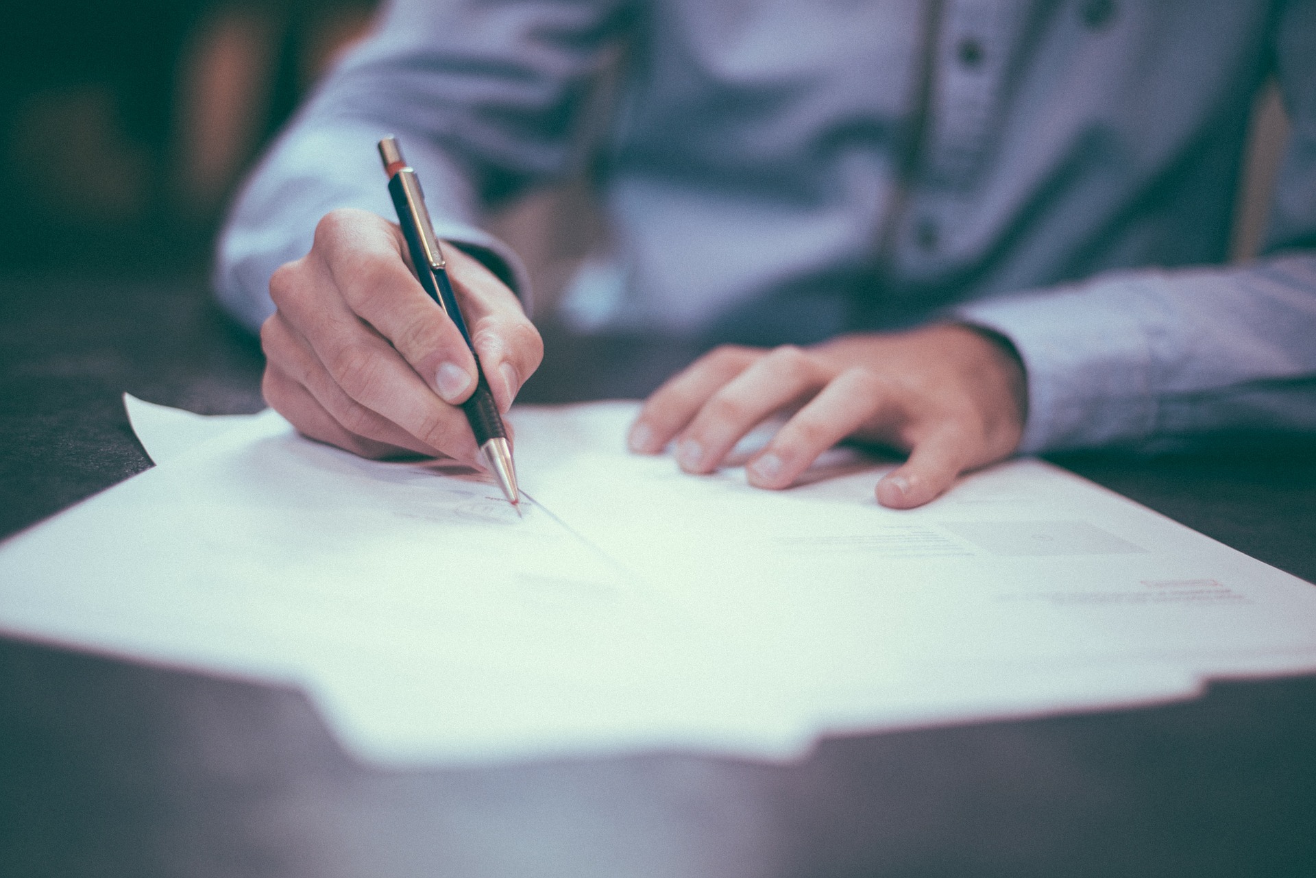 Man writes on a piece of paper with a mechanical pencil.