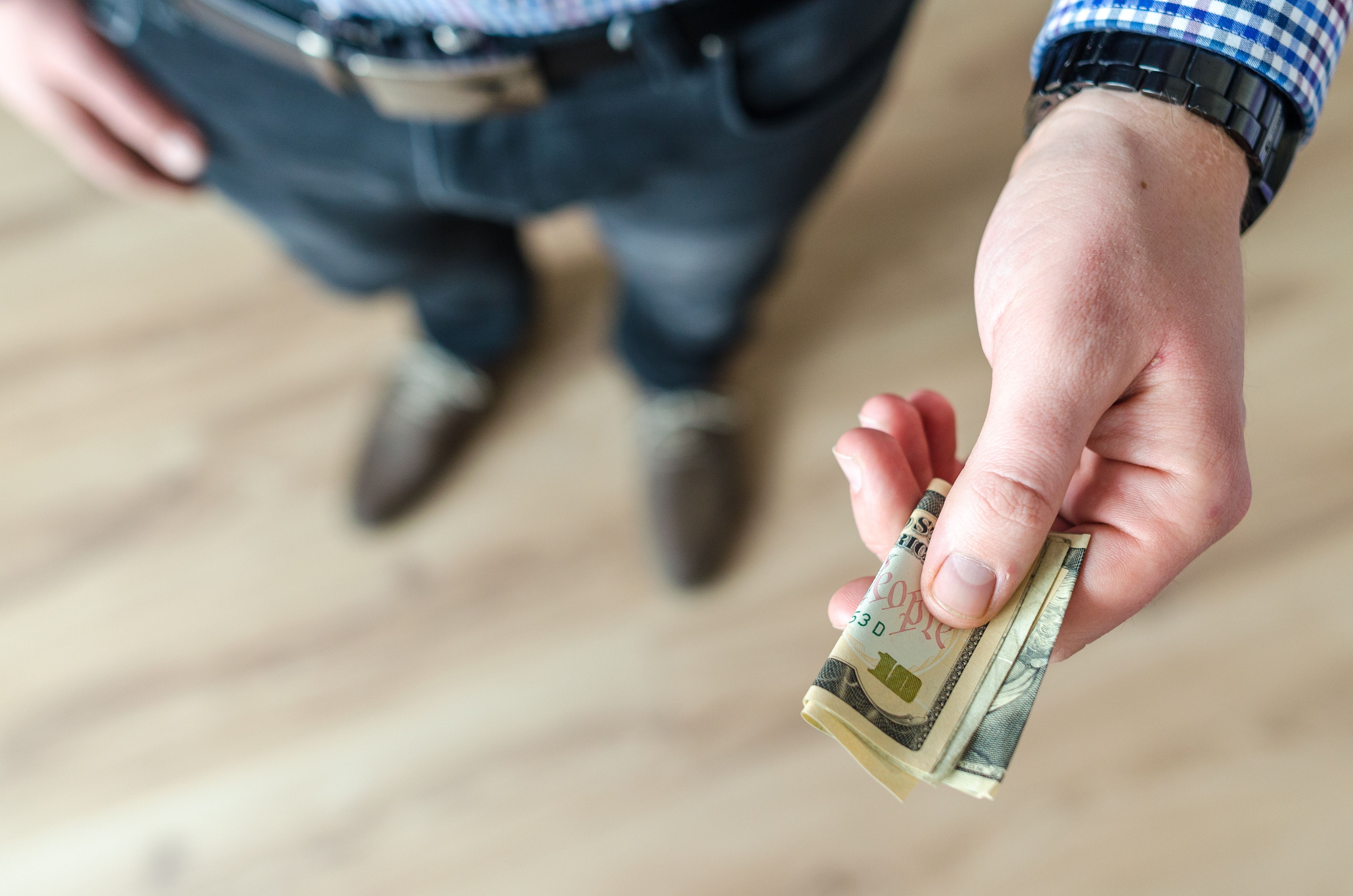 Man holds out a folded ten dollar bill.