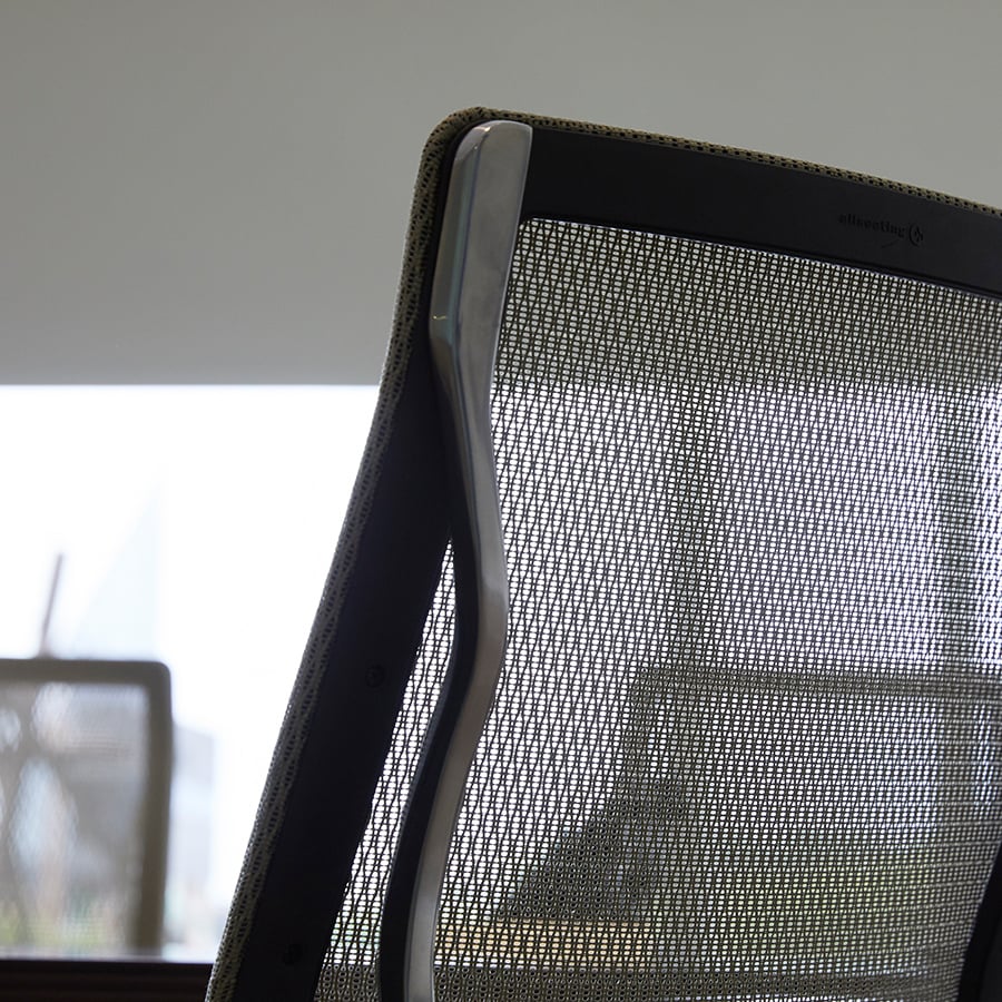 Detail of the net-like fabric back of a grey office chair.
