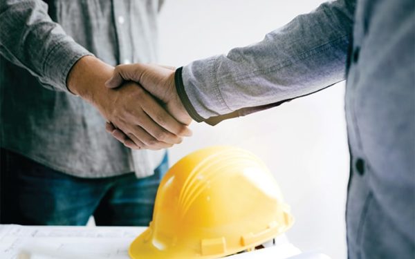 Two people shake hands above a yellow hard hat.