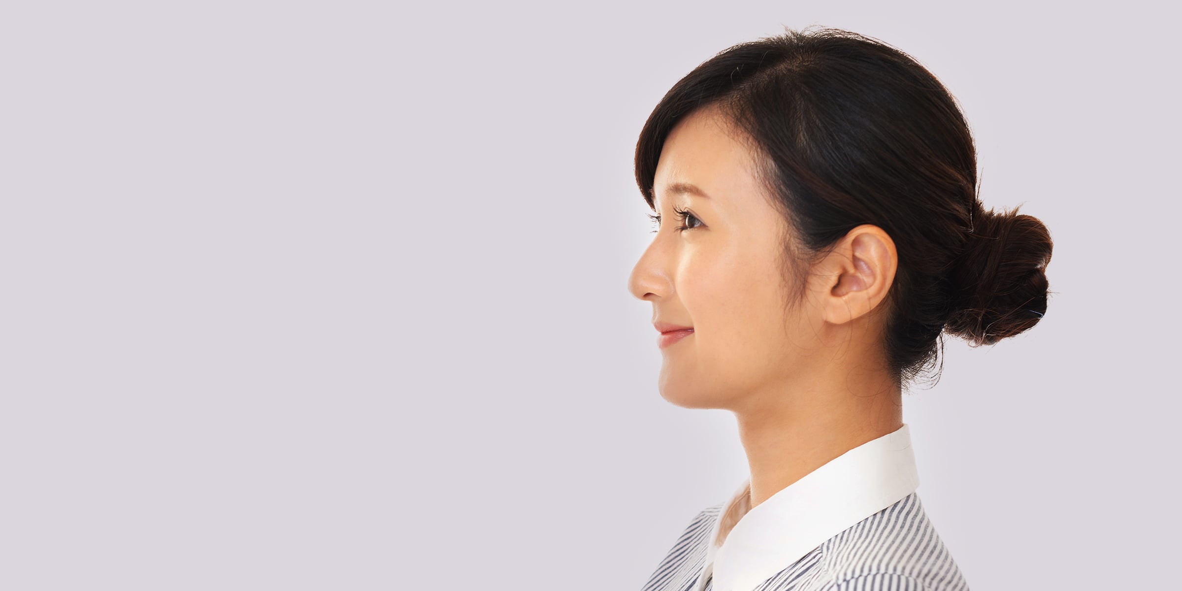 Profile of a brunette woman in a bun and white and blue striped shirt.