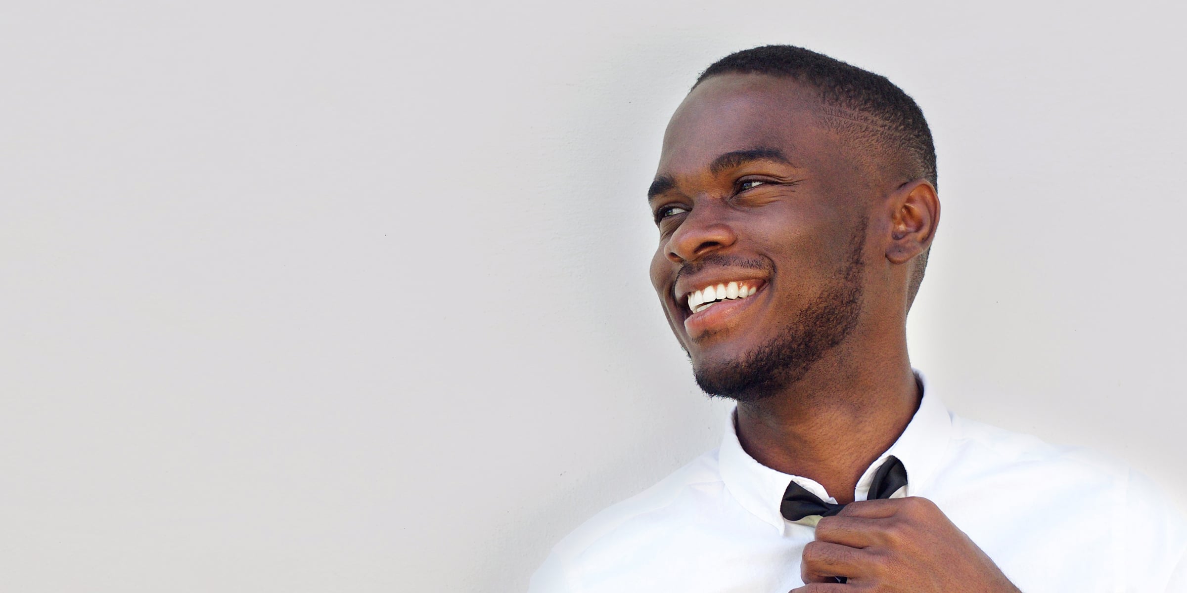 Smiling man in a white button up shirt adjusting his black tie.