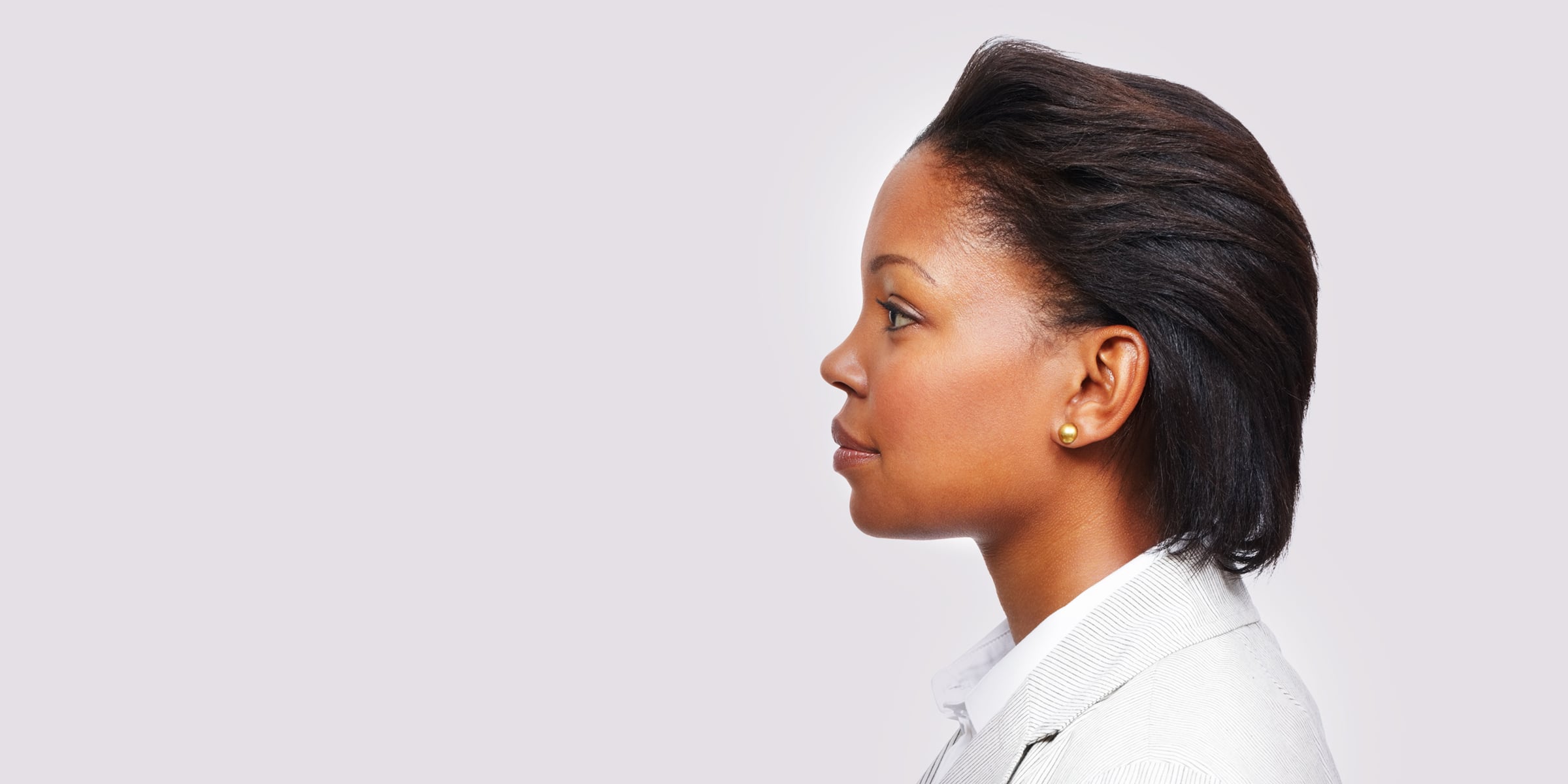 Profile of a black haired woman in a light gray blazer and white button up shirt.