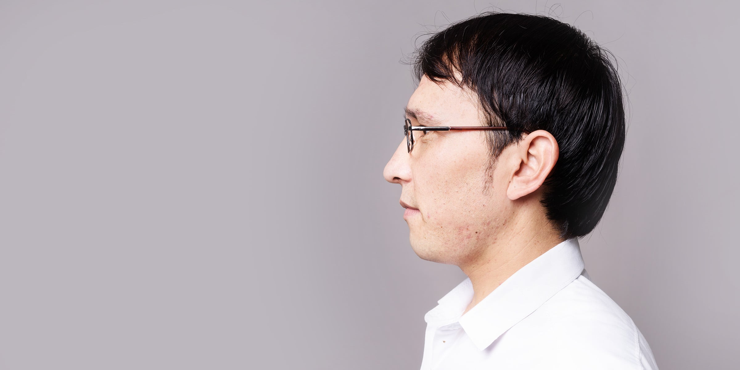 Profile of a black haired man in glasses and a white button up shirt.