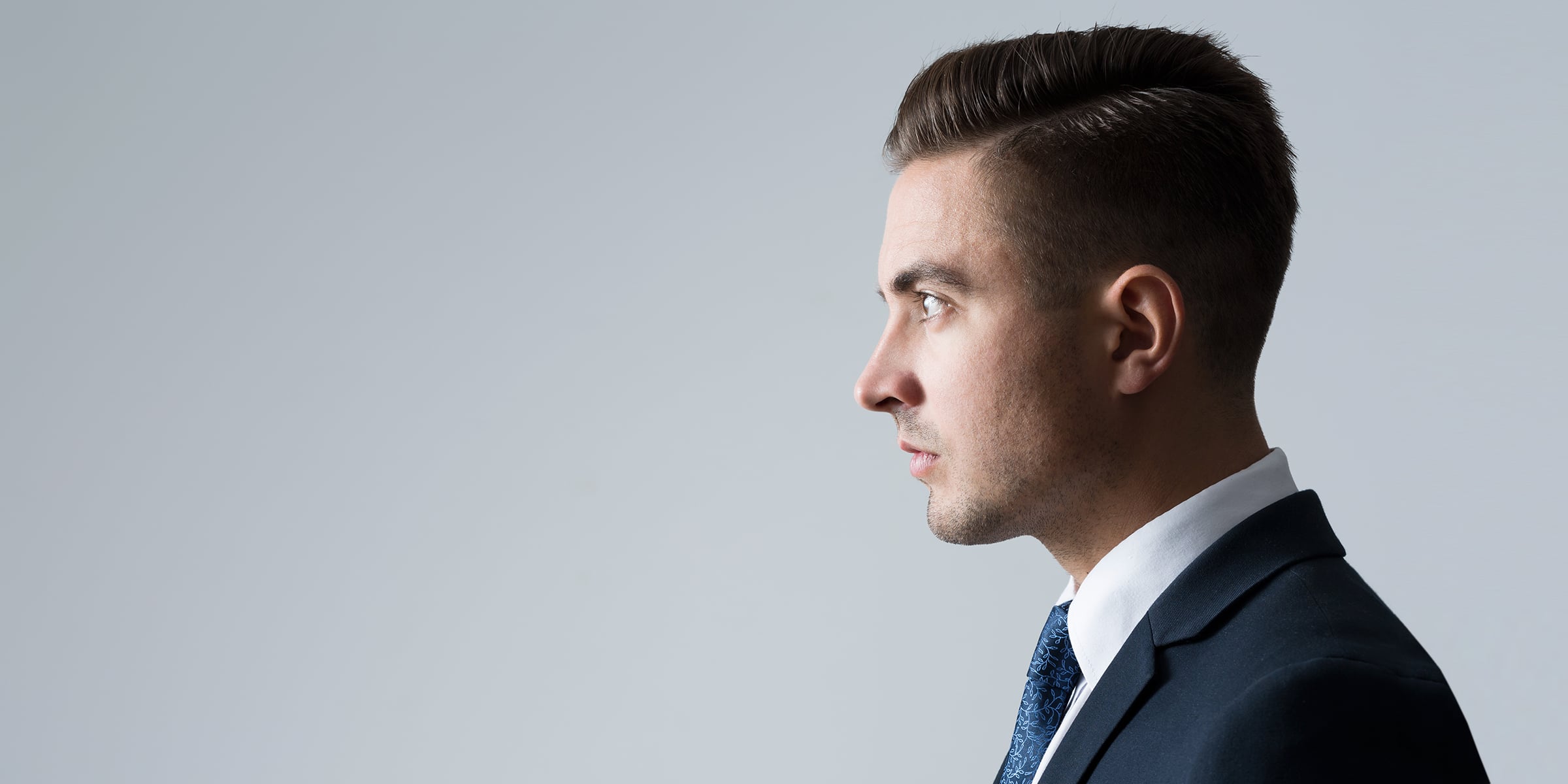 Profile of man wearing a blue blazer with hair slicked back.