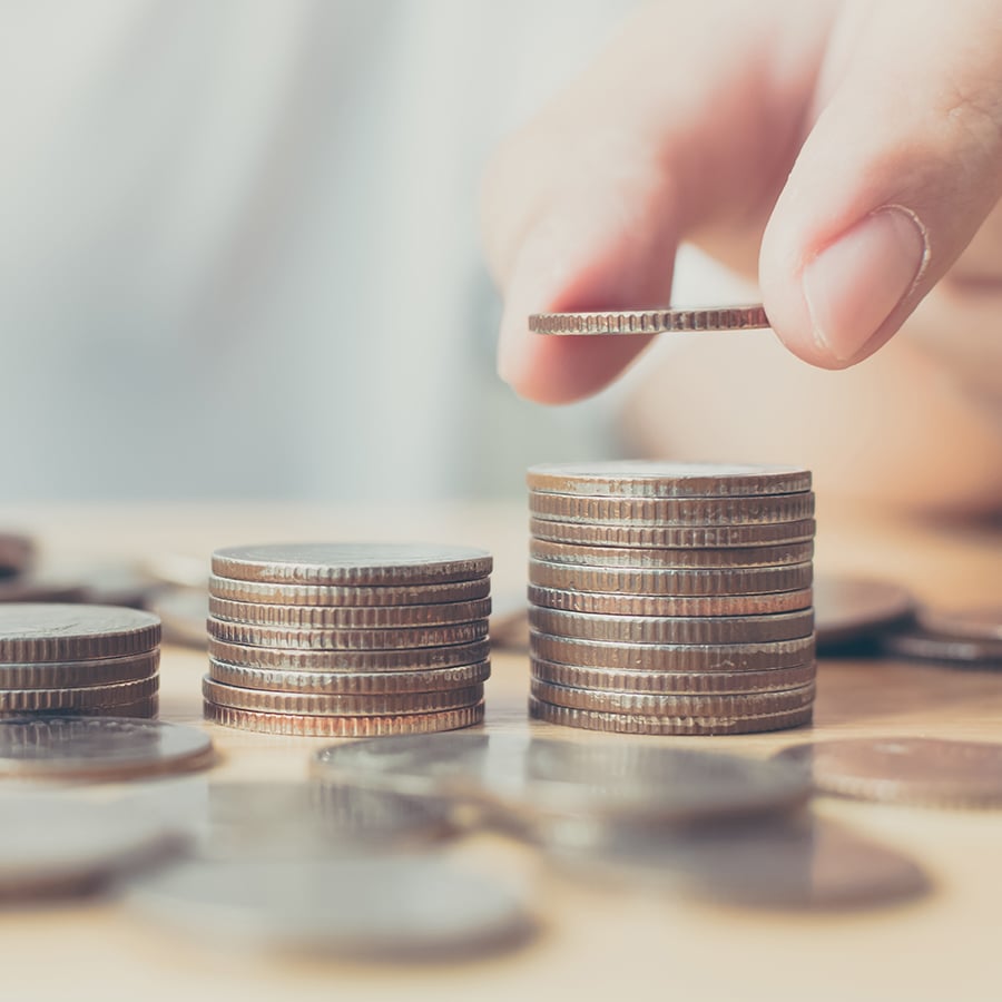 Hand places a coin on a taller stack of coins sitting next to two small stacks of coins.