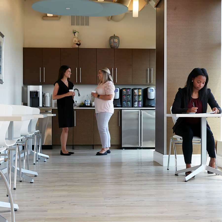 Two women stand in Ellin & Tucker's cafe area while another woman sits at a table working.