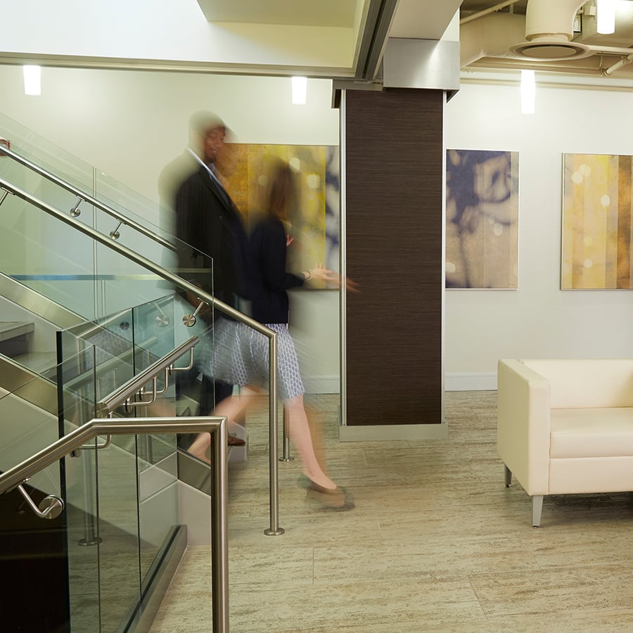 Two people walk down stairs into a cream colored lobby.