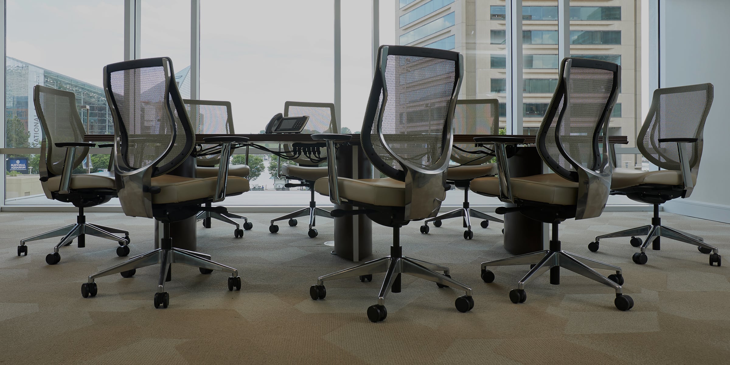 Conference room an oblong table with 4 beige and gray office chairs around it.