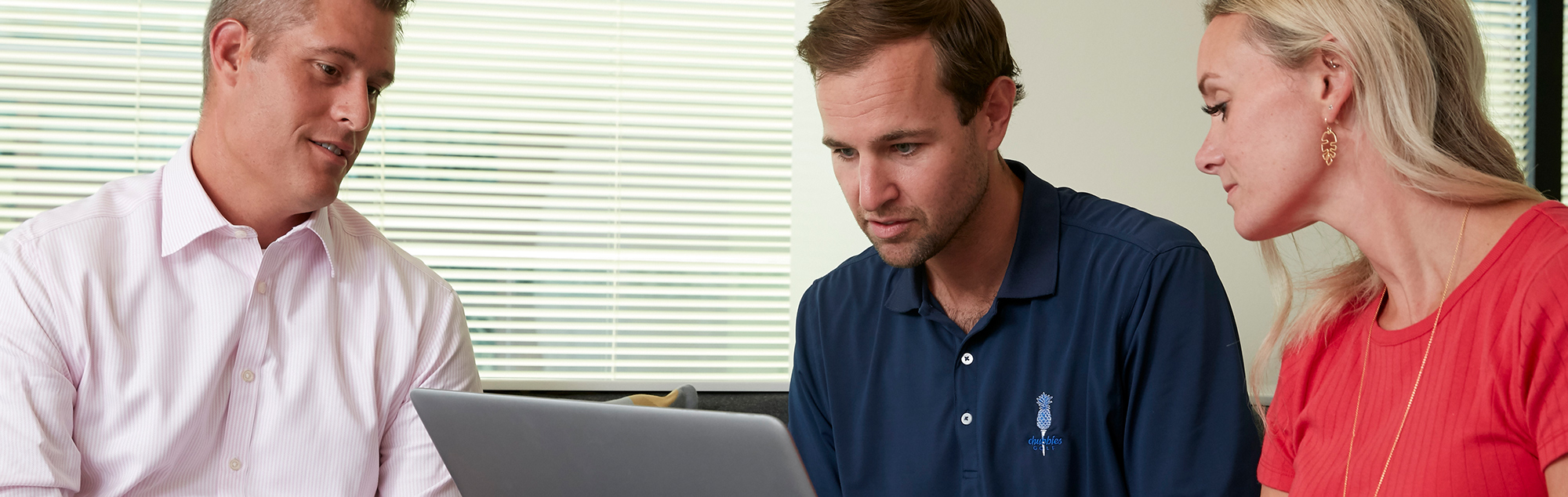 Two men and a woman sit and look at a laptop screen.