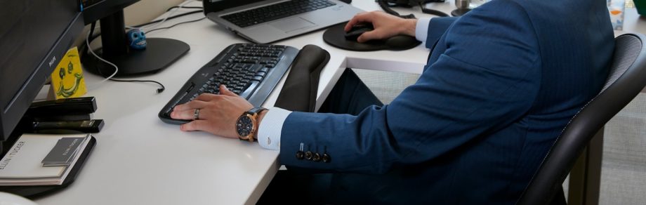 Man in blue suit sits while working at desk on computer.