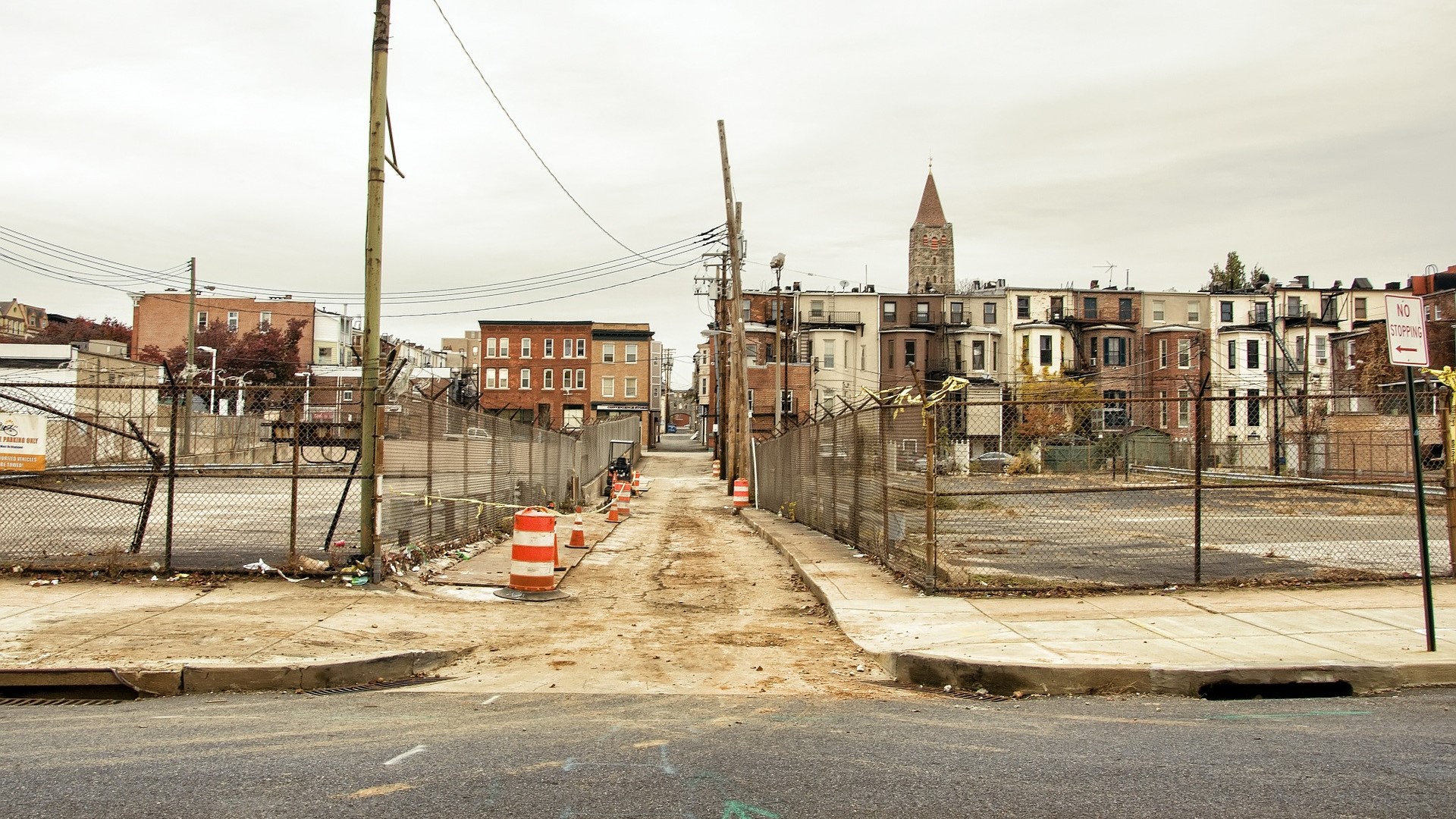 Two empty fenced off concrete lots in front of older looking rowhomes.