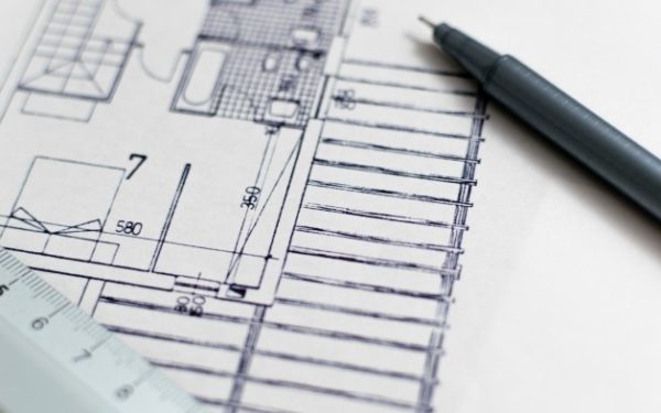 Corner of a blue print with a pen and ruler sitting on top.