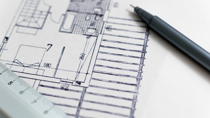 Corner of a blue print with a pen and ruler sitting on top.
