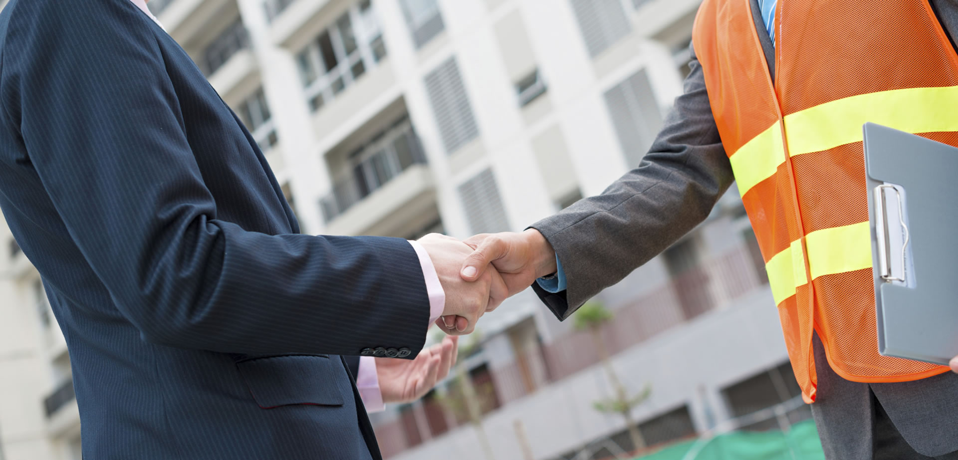 Man in suit shakes hand of man in suit wearing an orange vest and holding clipboard.