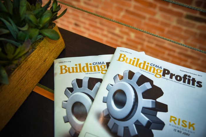 Two copies of CFMA Building Profits Magazine with on a table next to a plant in front of a brick wall.