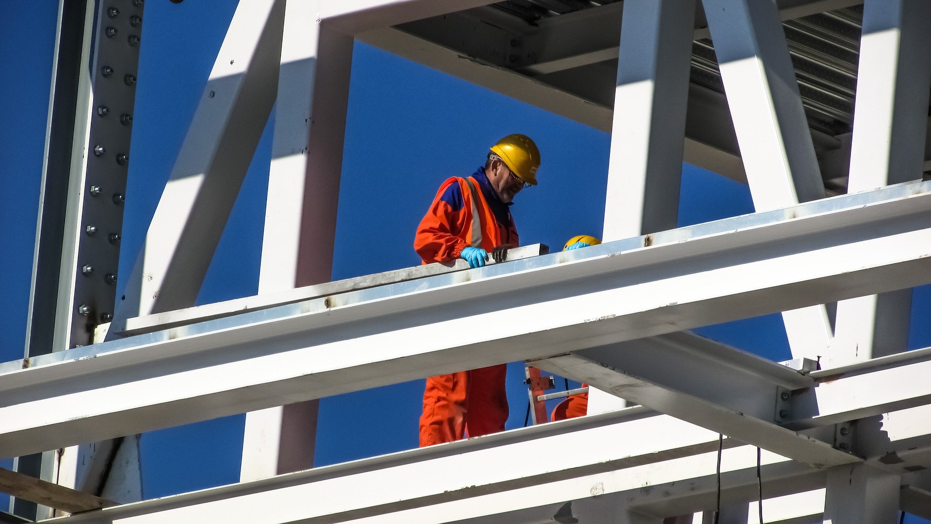Construction worker in orange jumpsuit on white scaffolding.