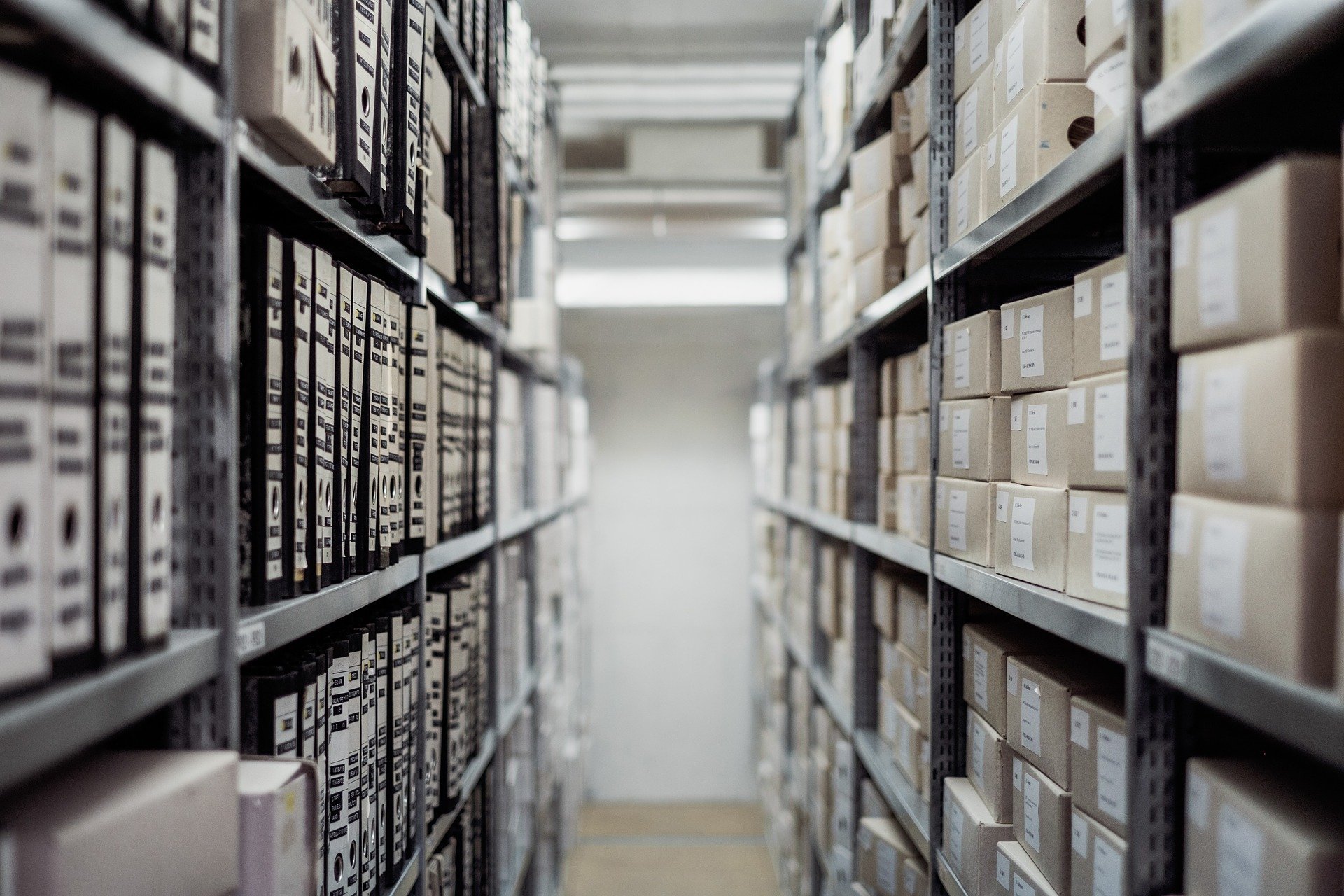 Aisle of storage shelves with labeled boxes and binders on either side.