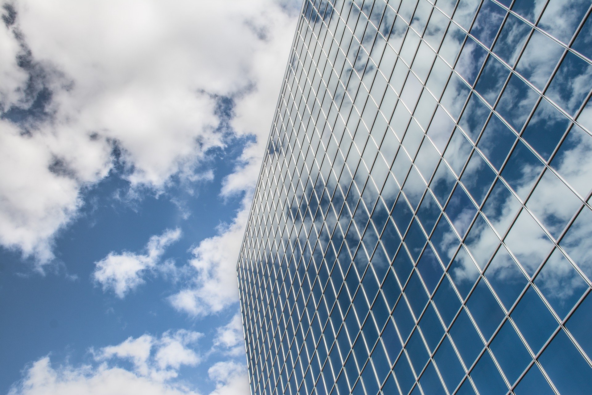 Blue sky with clouds and it's reflection in a gridded reflective building.