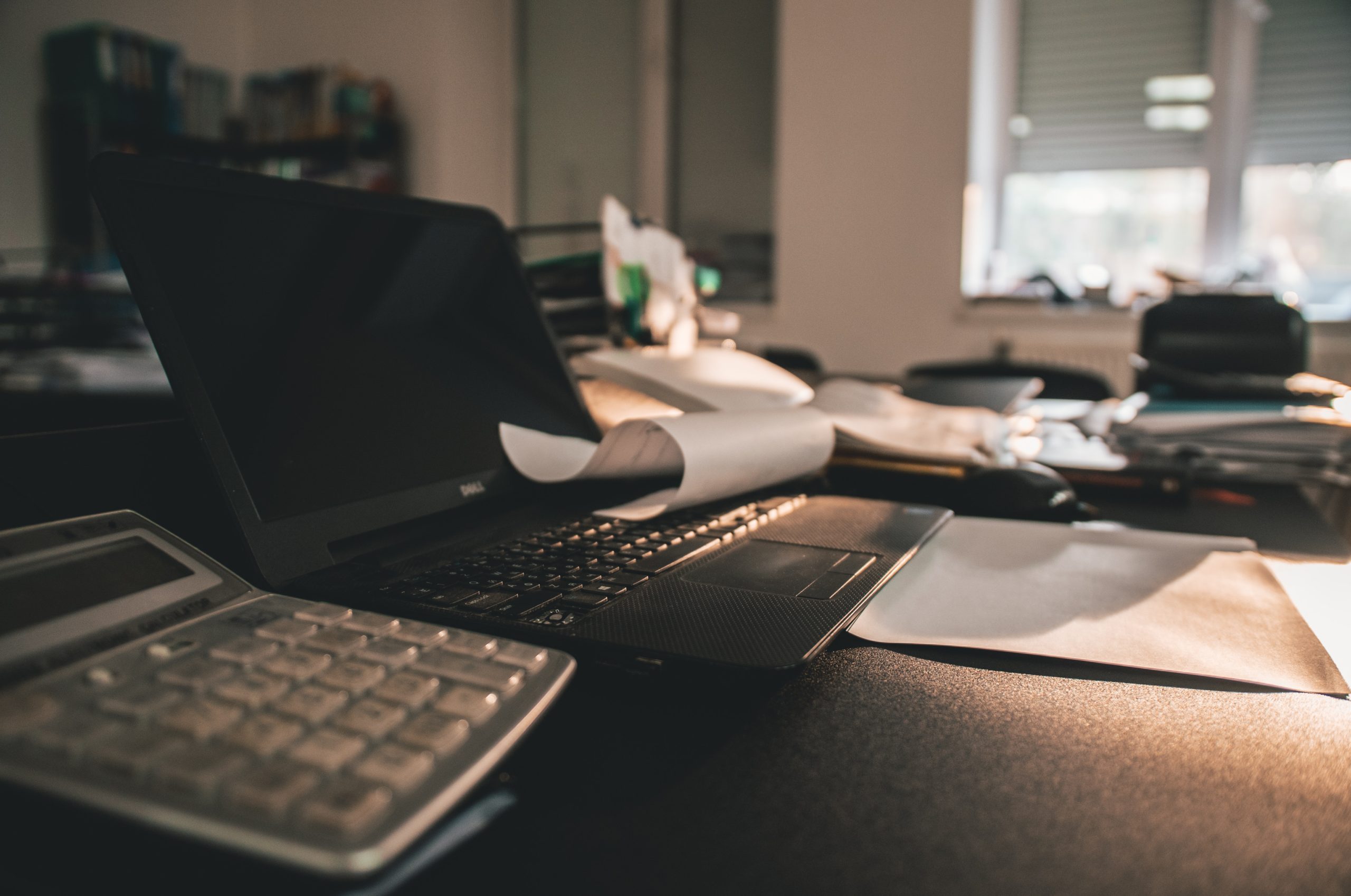 Calculator and laptop sitting on dimly lit desk in office.