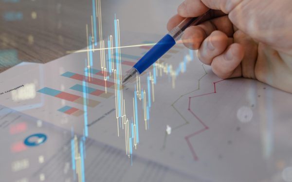 Hand holds a pen on top of a paper with graphs with a low opacity overlay of a line graph.