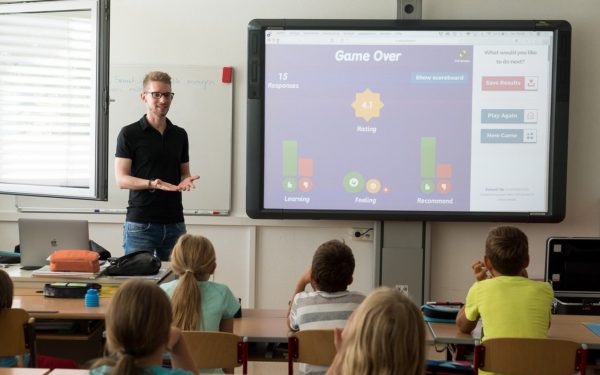 Teacher standing in front of classroom of students sitting at desks.