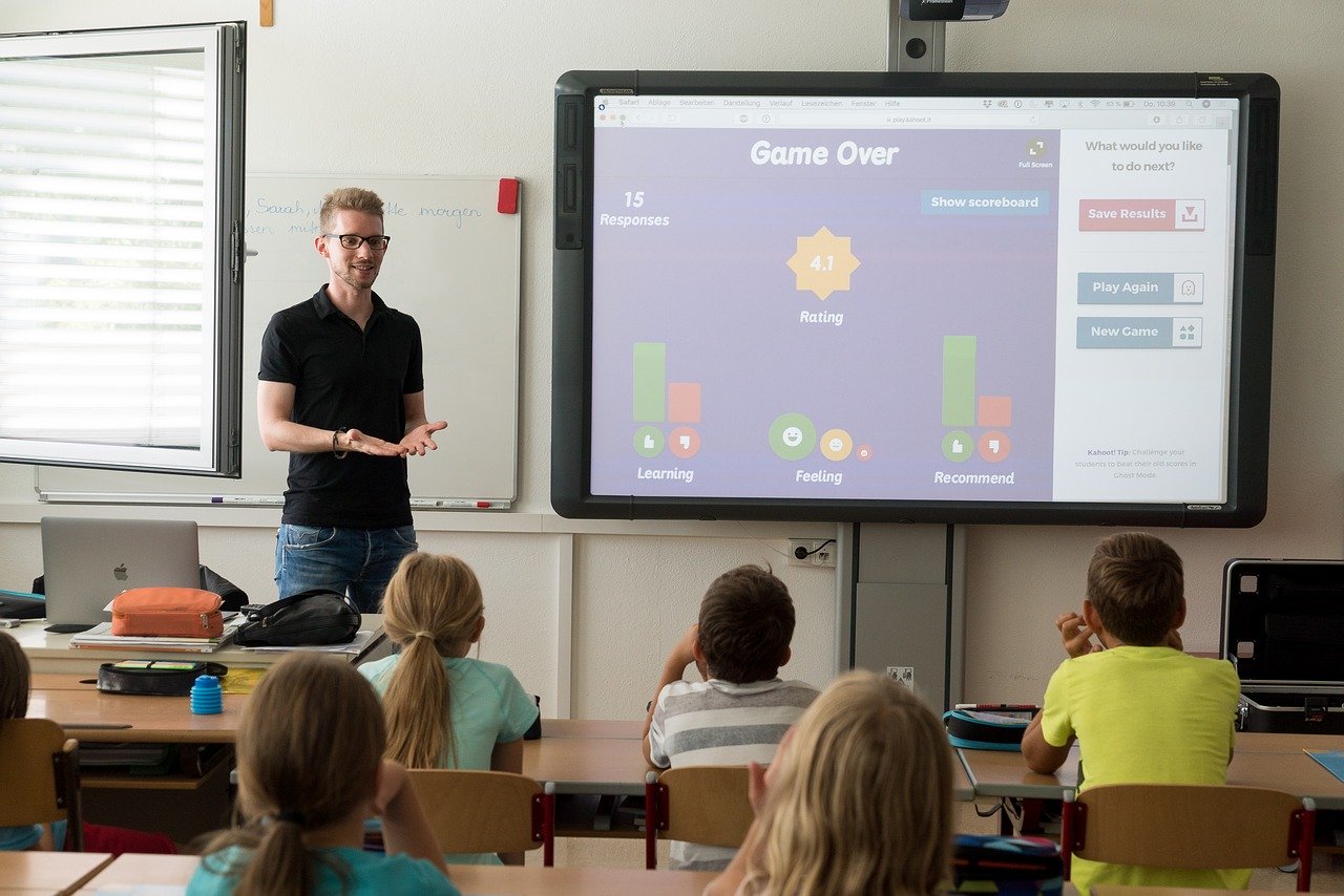 Teacher standing in front of classroom of students sitting at desks.