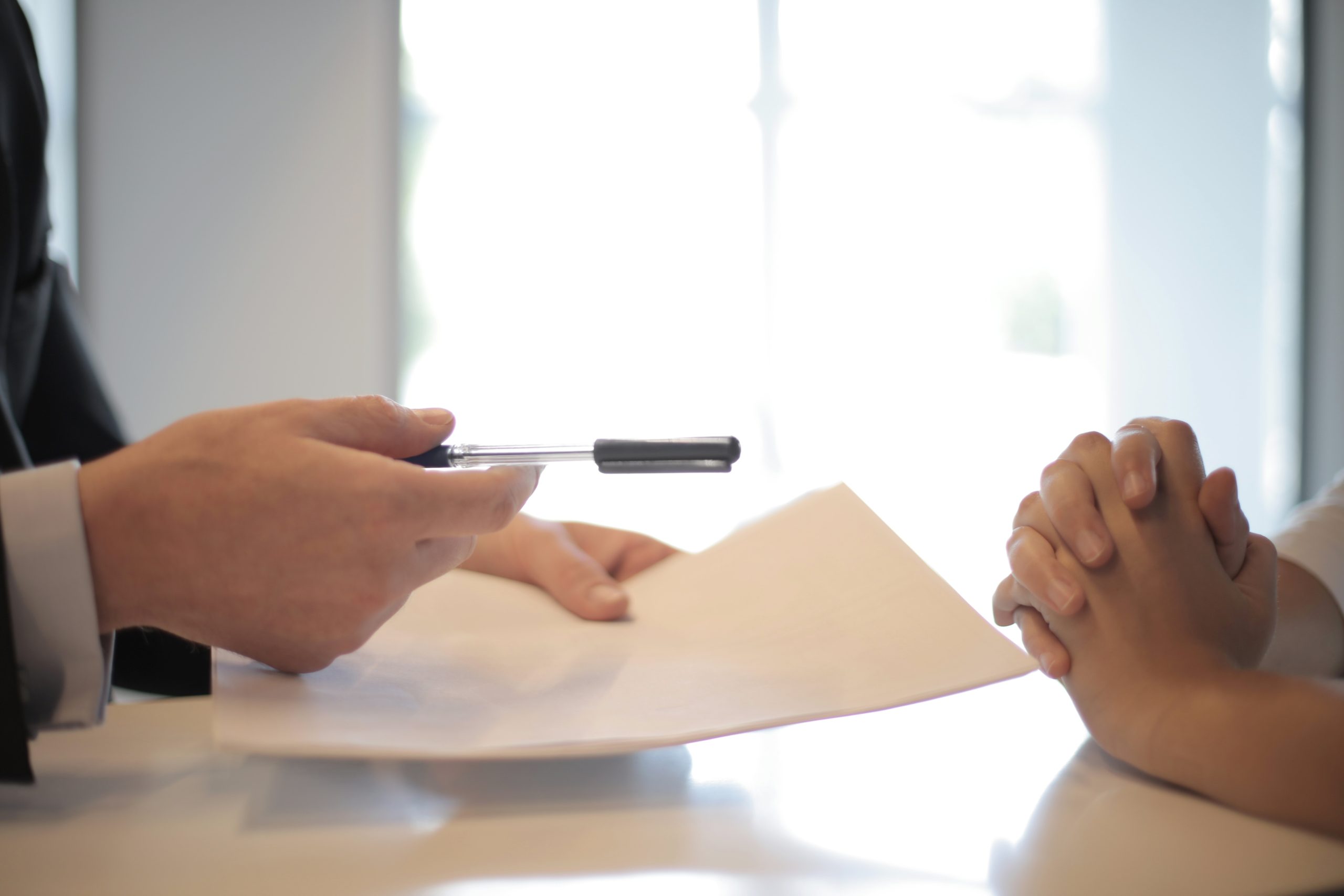 Hands holding paper and pen sitting across from a pair of folded hands.