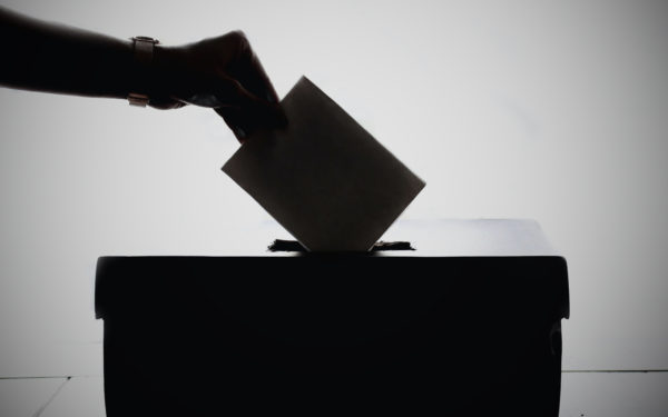 Silhouette of hand putting paper in ballot box.