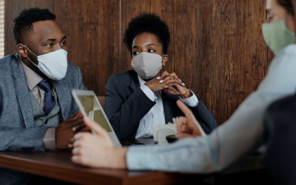 Three business people sitting at table wearing masks.