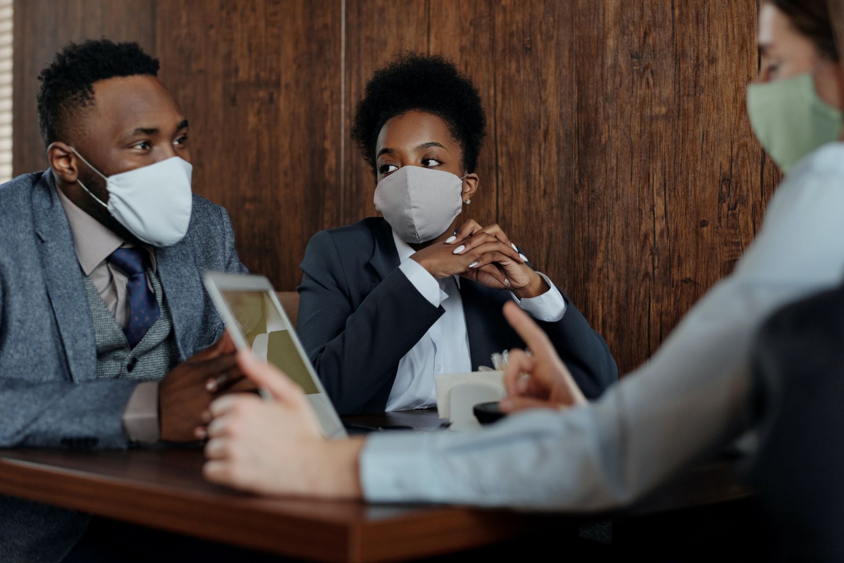 Three business people sitting at table wearing masks.