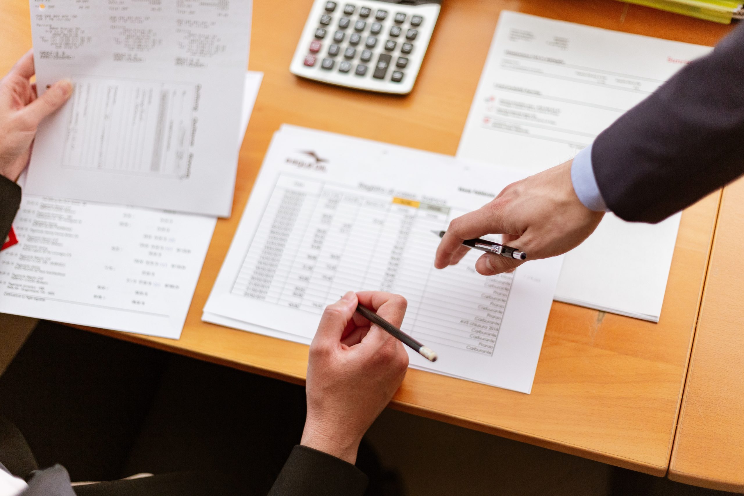 Desk with papers and two men's hands pointing.