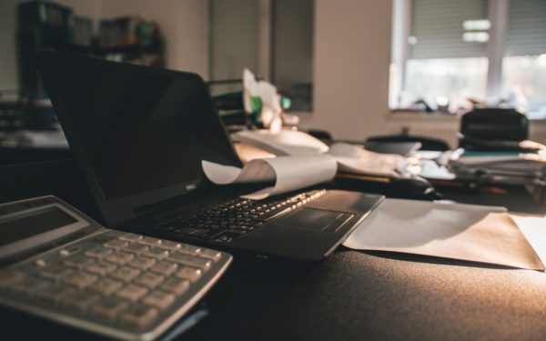 Laptop on desk with papers in dimly lit office.