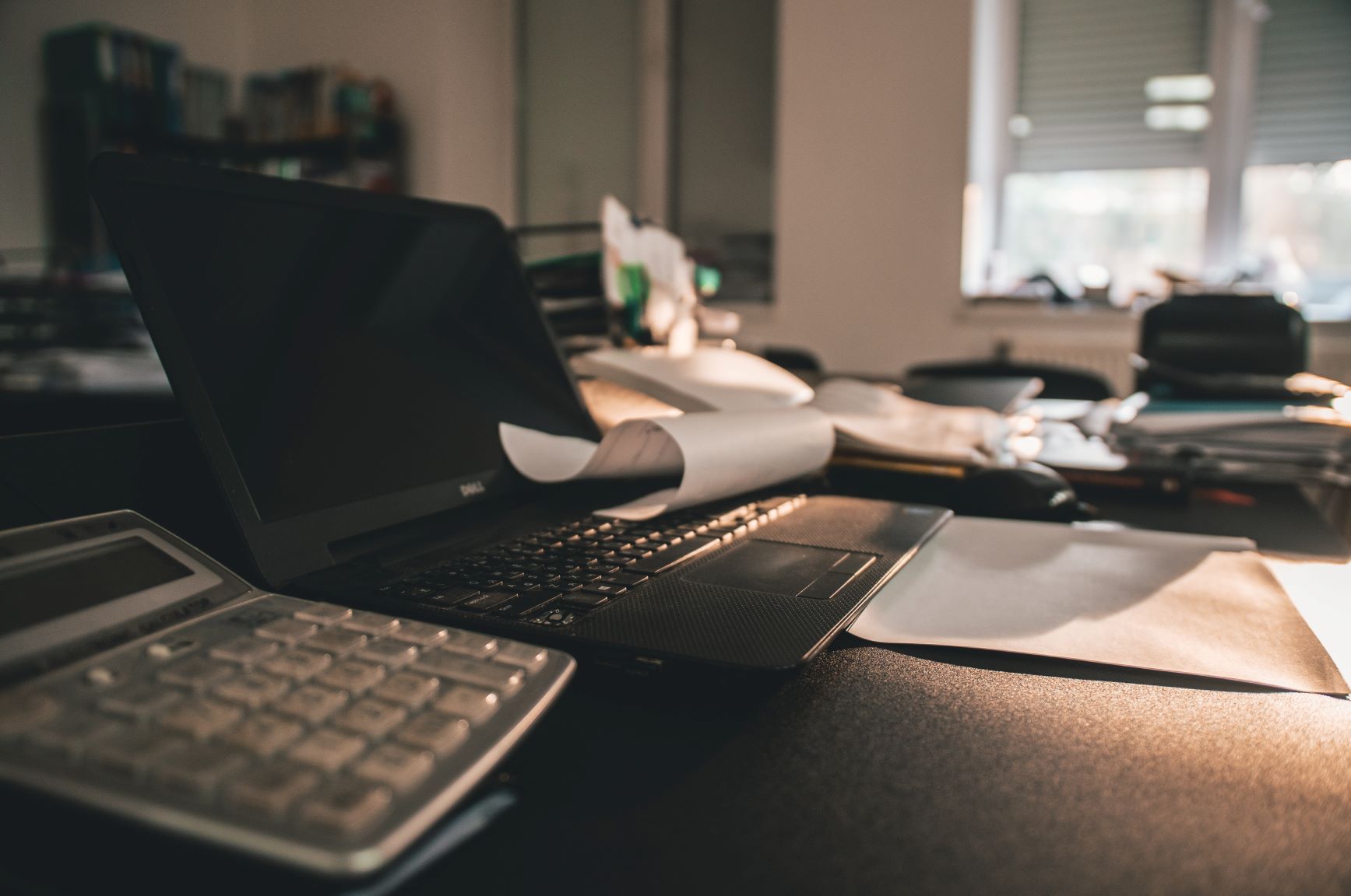 Laptop on desk with papers in dimly lit office.