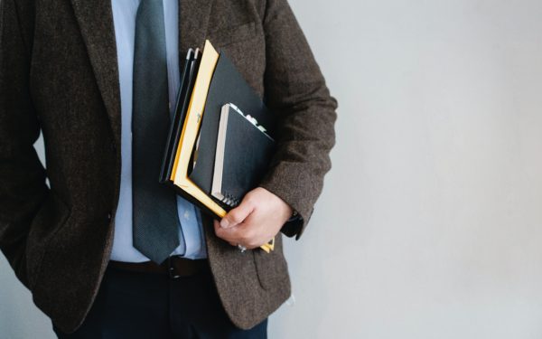 Man in wool blazer holding notebook and paperwork under his arm.