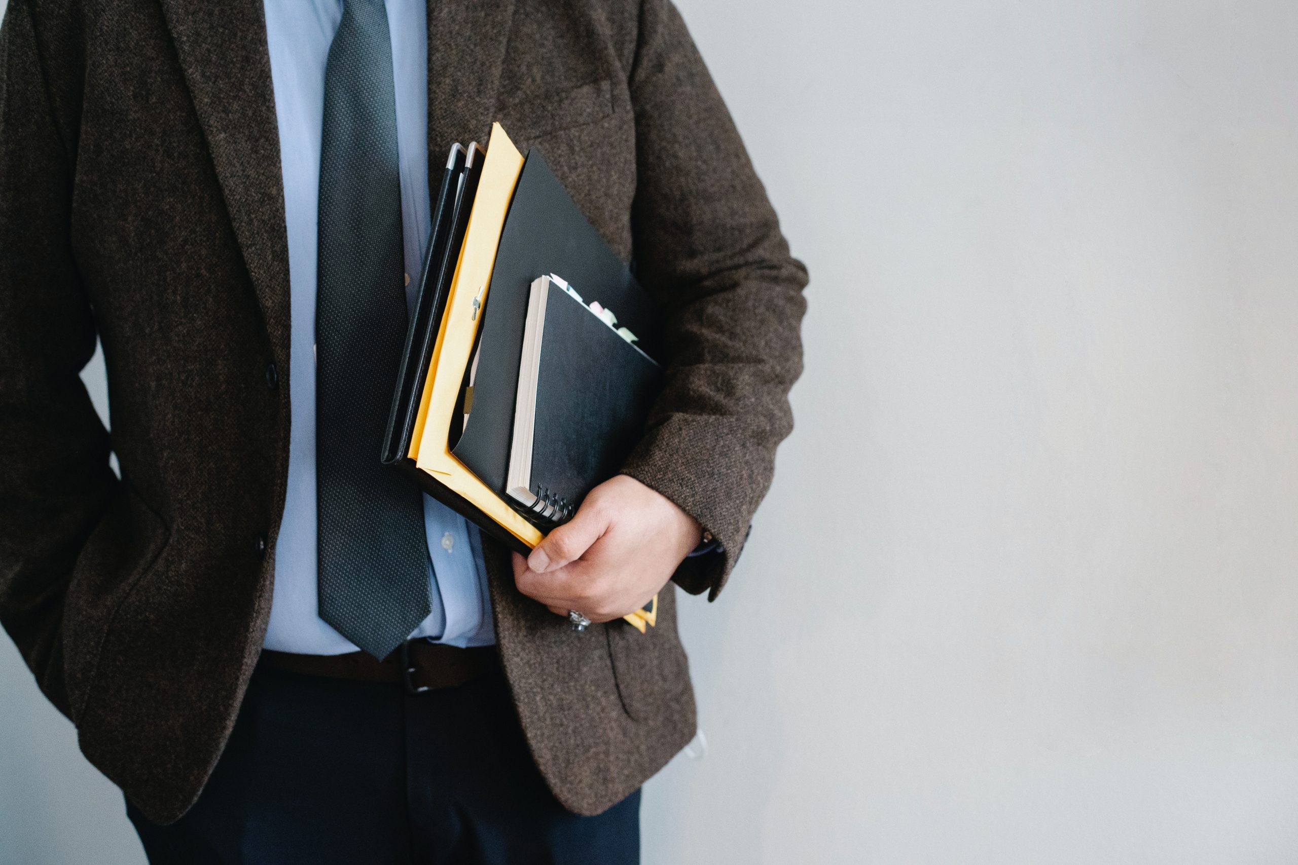 Man in wool blazer holding notebook and paperwork under his arm.