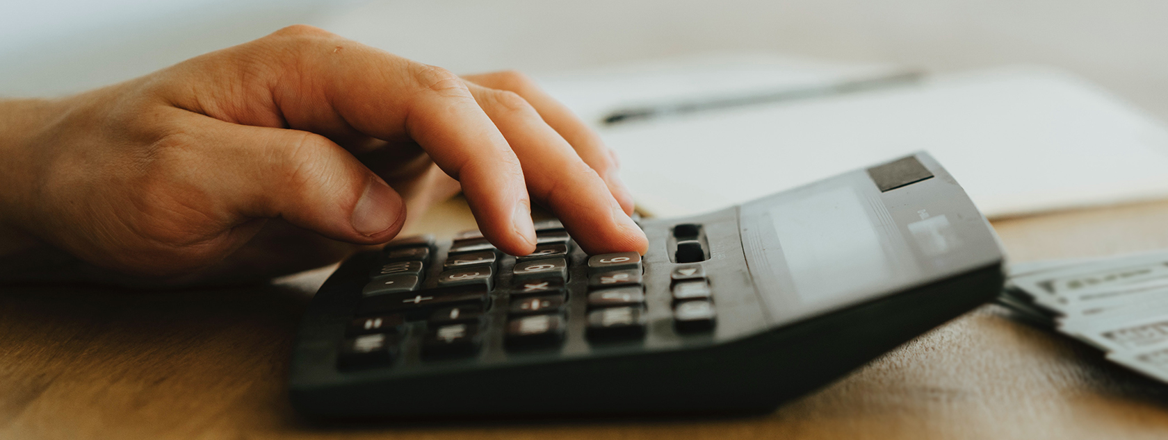 Hand typing on calculator sitting on desk.