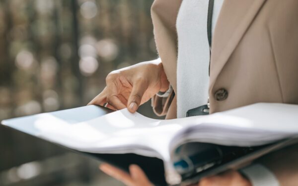 Woman in beige coat holding binder of papers.