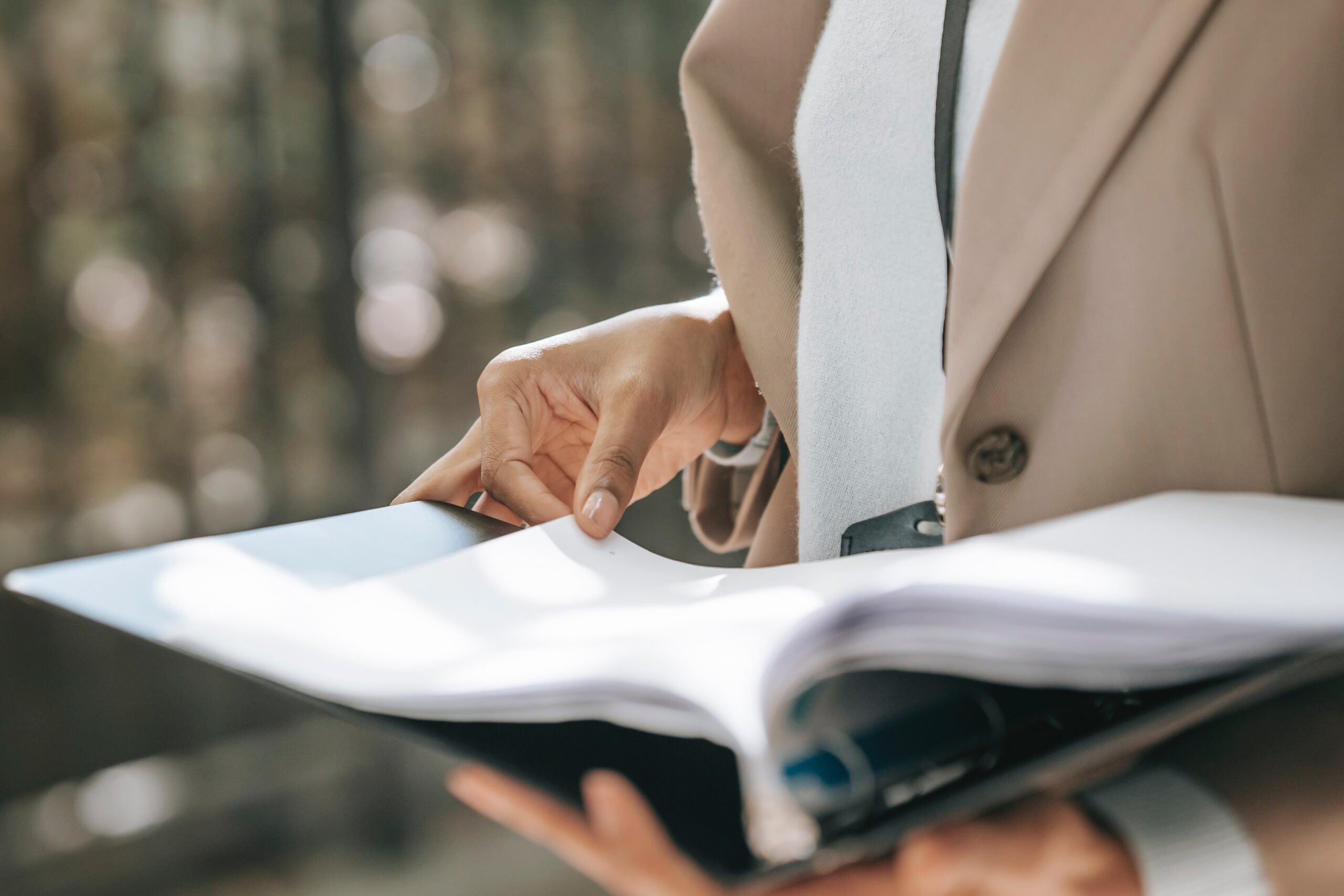 Woman in beige coat holding binder of papers.