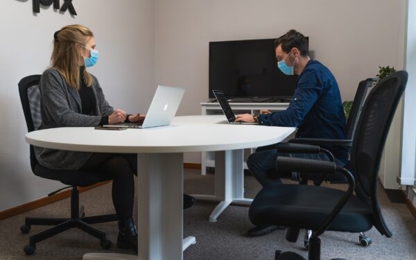 Man and woman sitting at conference table working and wearing masks.