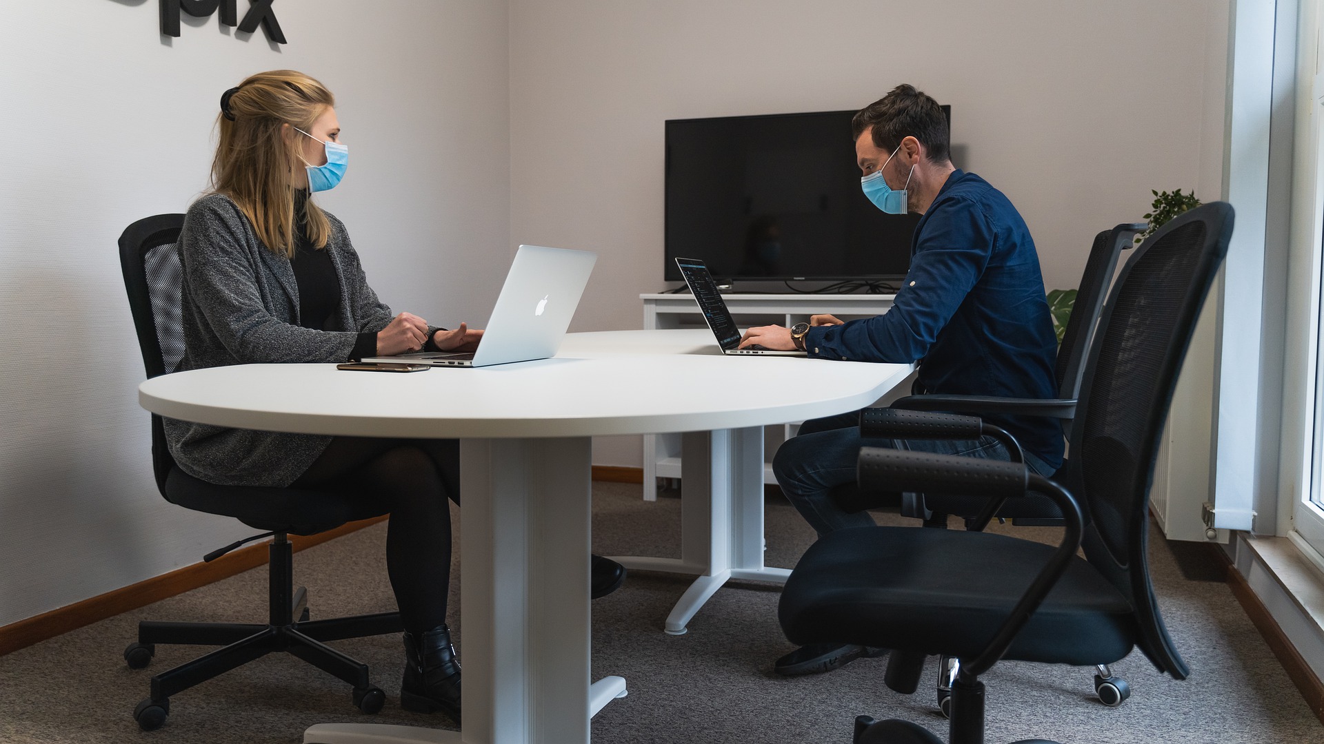 Man and woman sitting at conference table working and wearing masks.