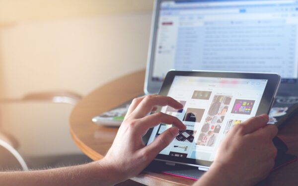 Person scrolling on tablet with computer screen in background.