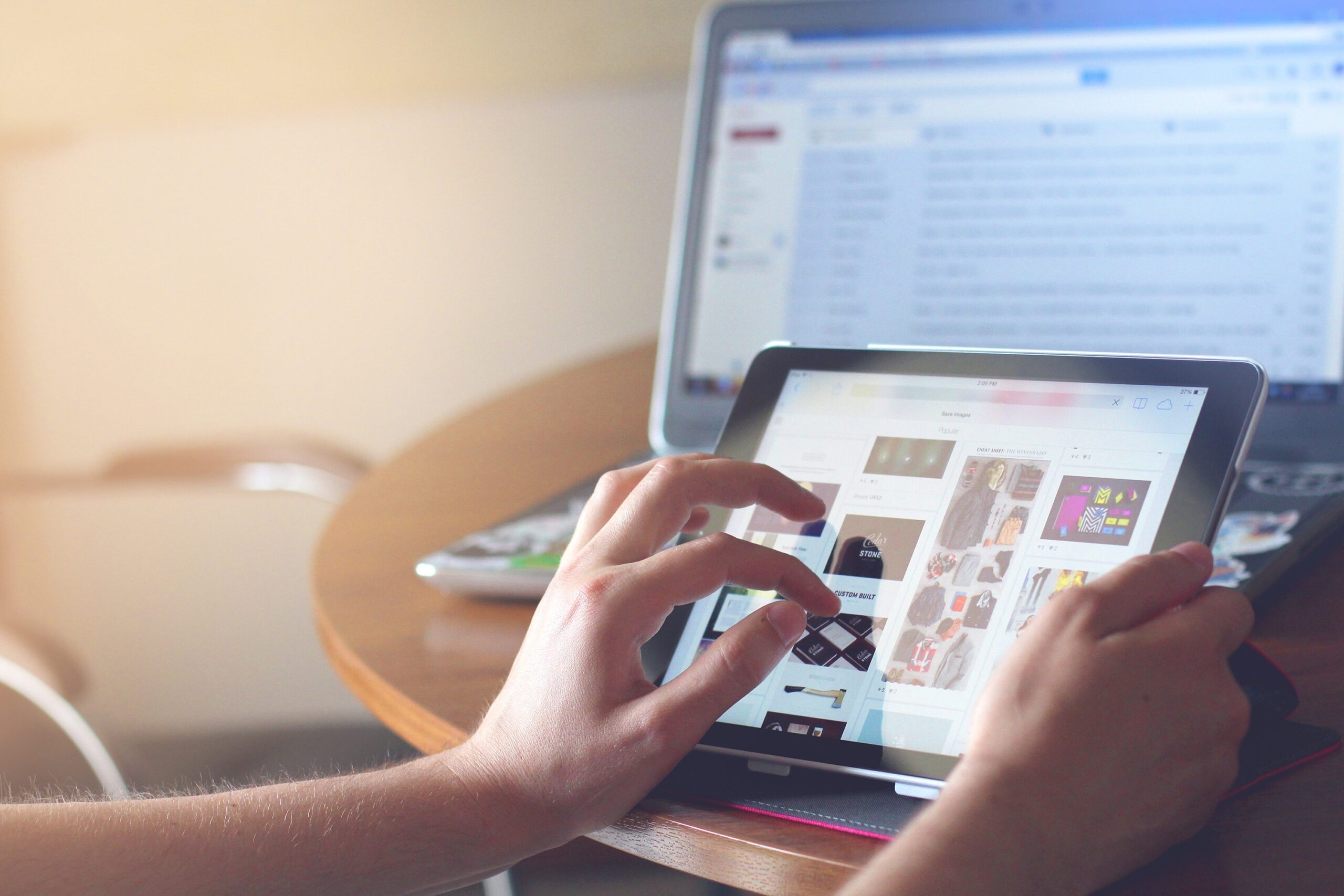 Person scrolling on tablet with computer screen in background.