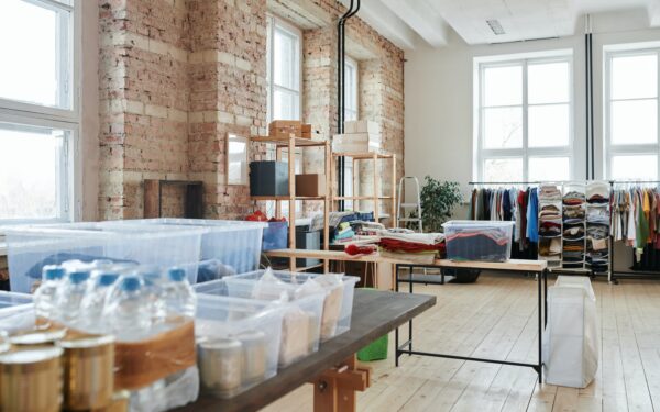 Large room full of clothing donations hanging on racks and sorted into plastic bins.