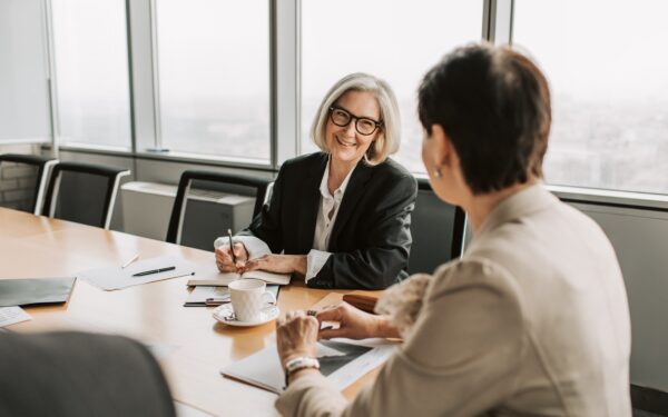 Two business women sitting at conference table talking.