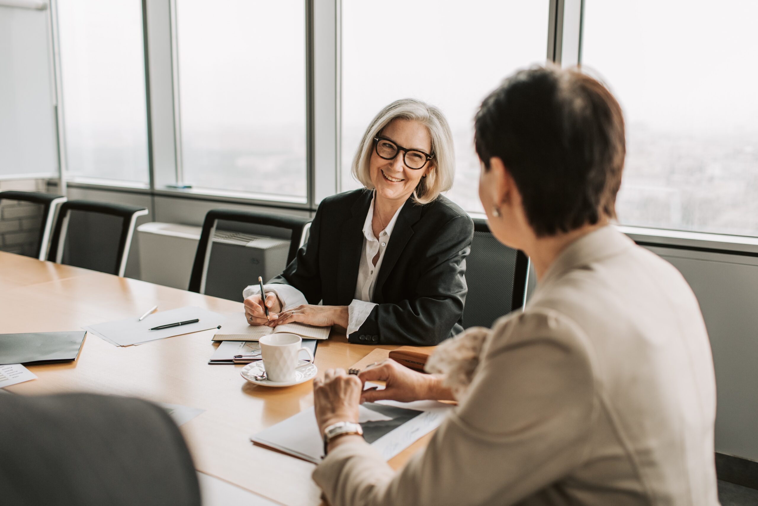 Two business women sitting at conference table talking.