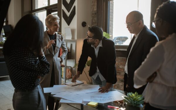 Group of people standing around desk looking at blueprint of office.