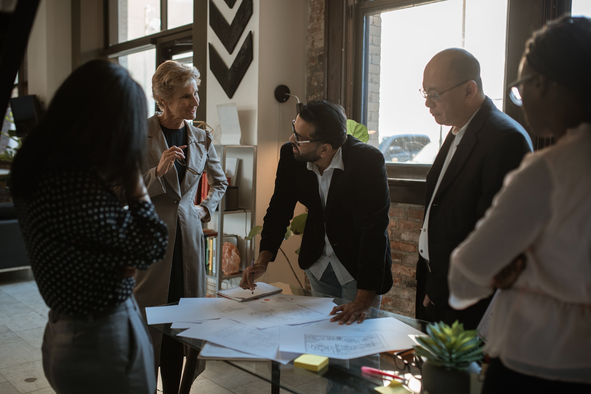 Group of people standing around desk looking at blueprint of office.