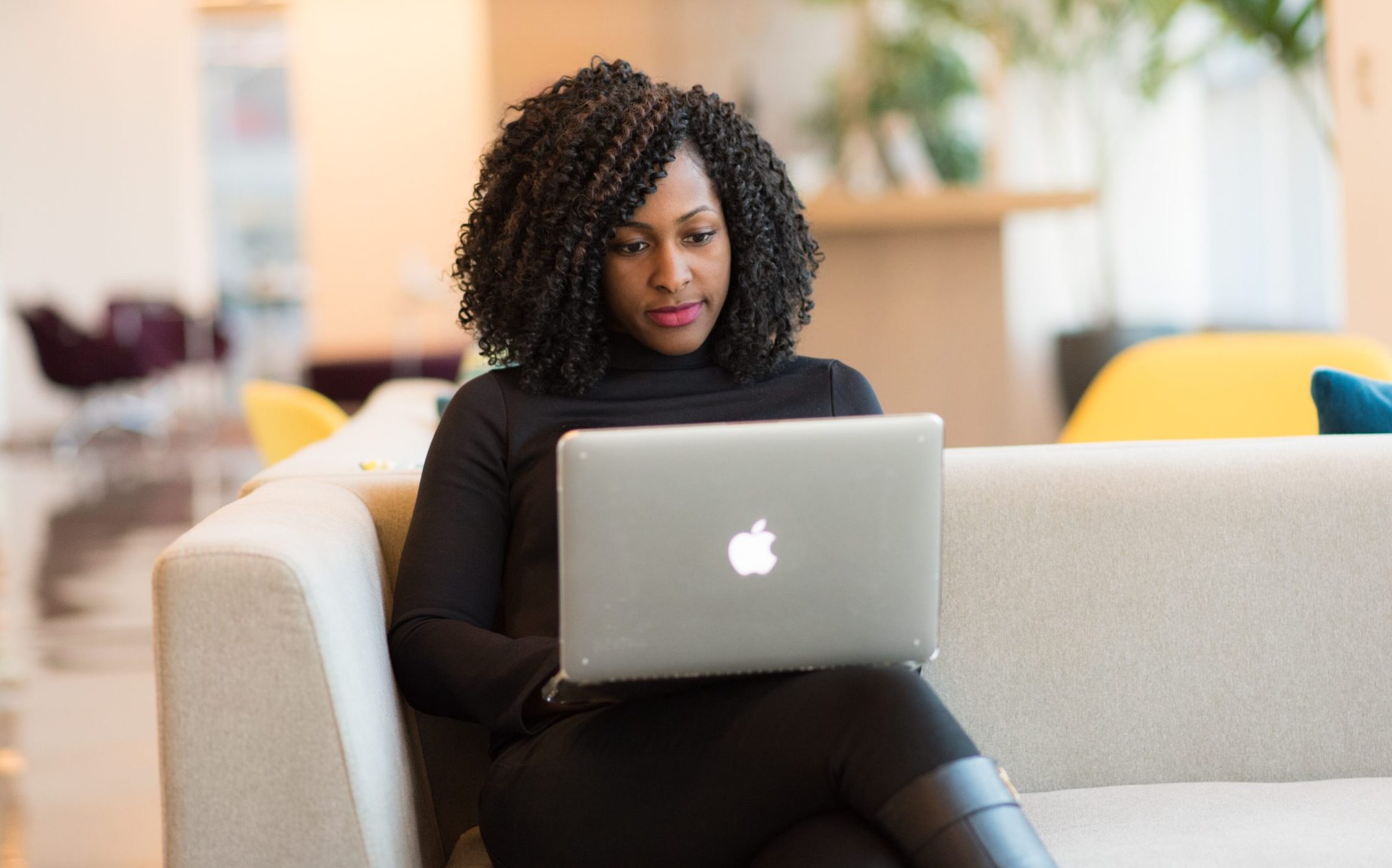 Woman sitting on coach holding MacBook.